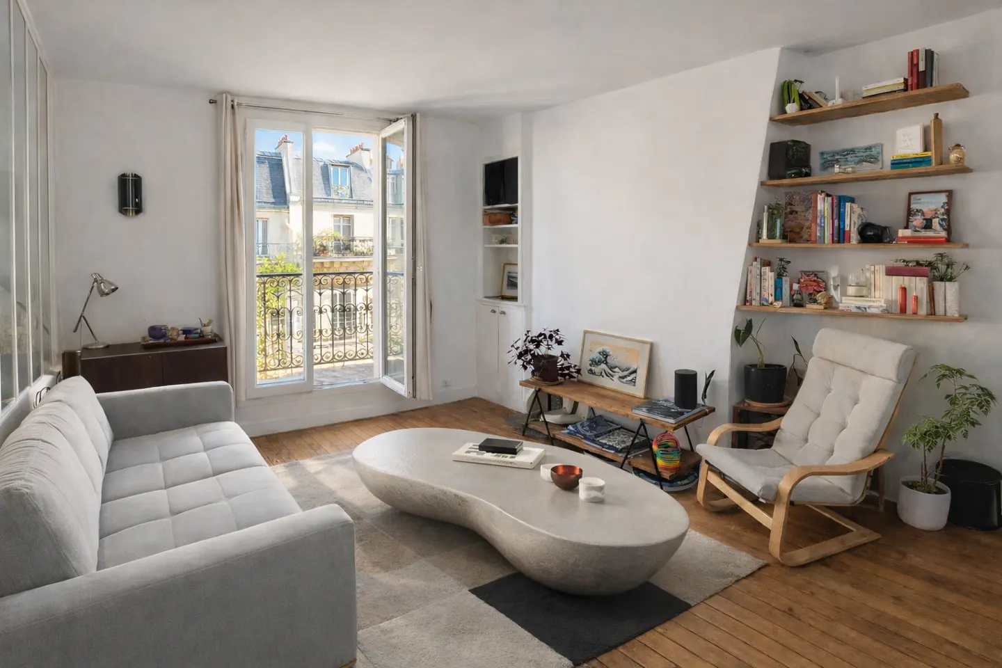 Bright living room with a gray sofa, unique coffee table, and open window showing a Parisian balcony. Bookshelves and a comfy chair add charm.