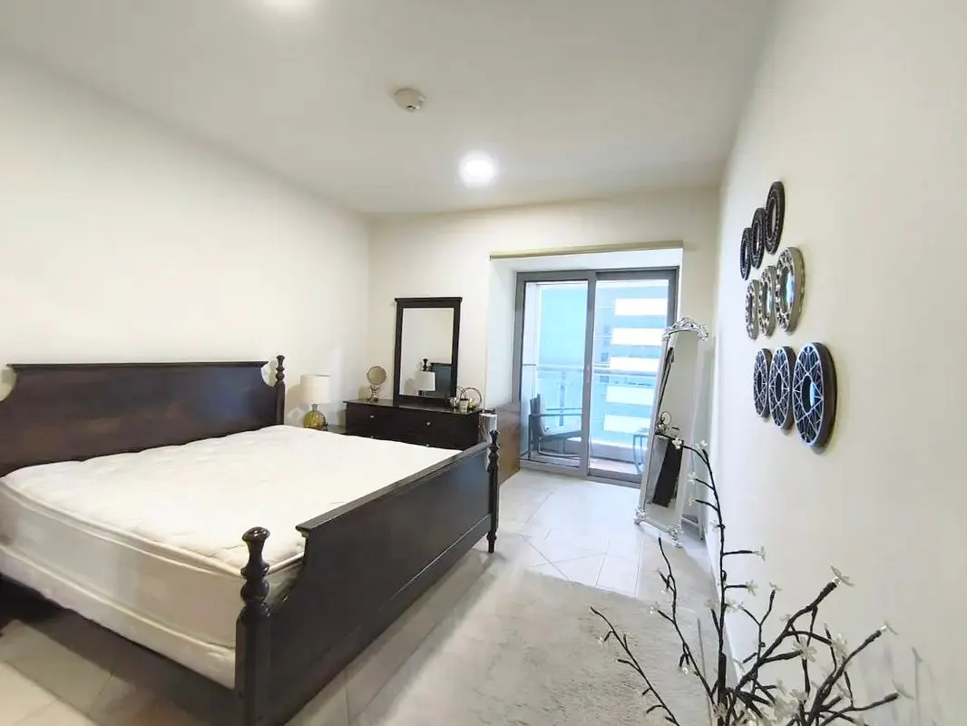 A bright bedroom with a dark wood bed, dresser, and balcony access. Decorative mirrors adorn the wall.