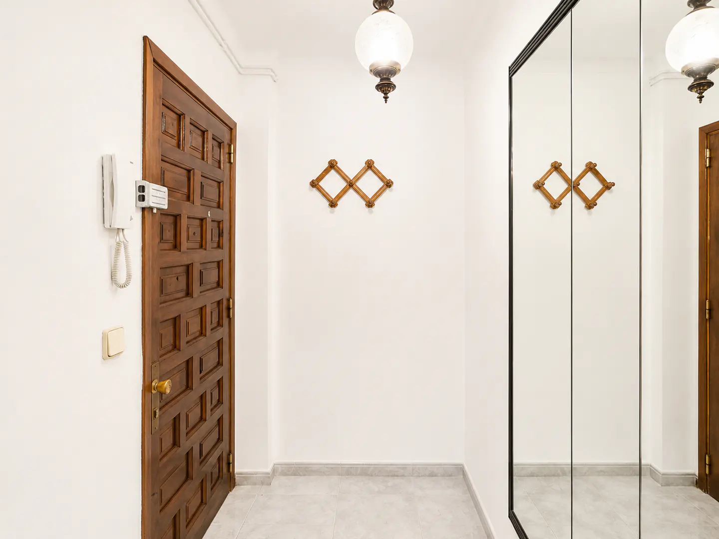 Bright hallway with a dark wood door, a mirrored closet, and a globe pendant light. A wooden coat rack hangs on the white wall.
