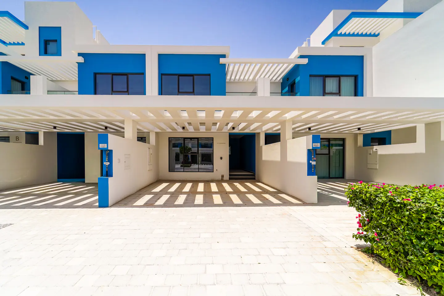 Exterior view of modern white townhouses with blue accents and covered parking on a sunny day.