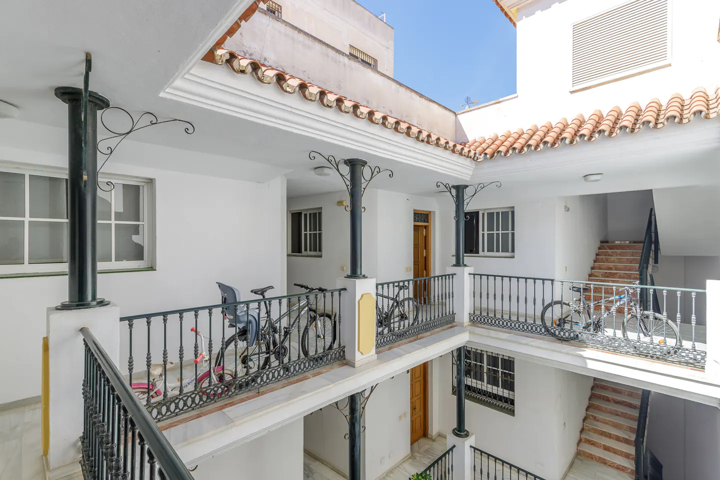 Courtyard view of a white building with black railings, columns, and bicycles parked on the balconies. Stairs are visible.