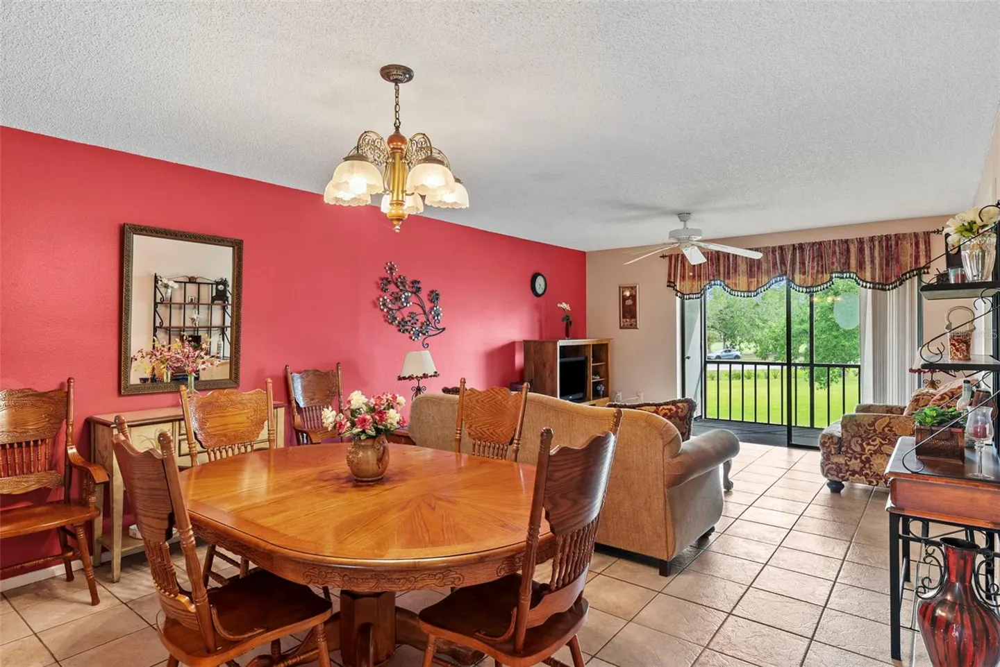 A living and dining area with a red accent wall, wooden table and chairs, and a view of a green lawn through sliding glass doors.