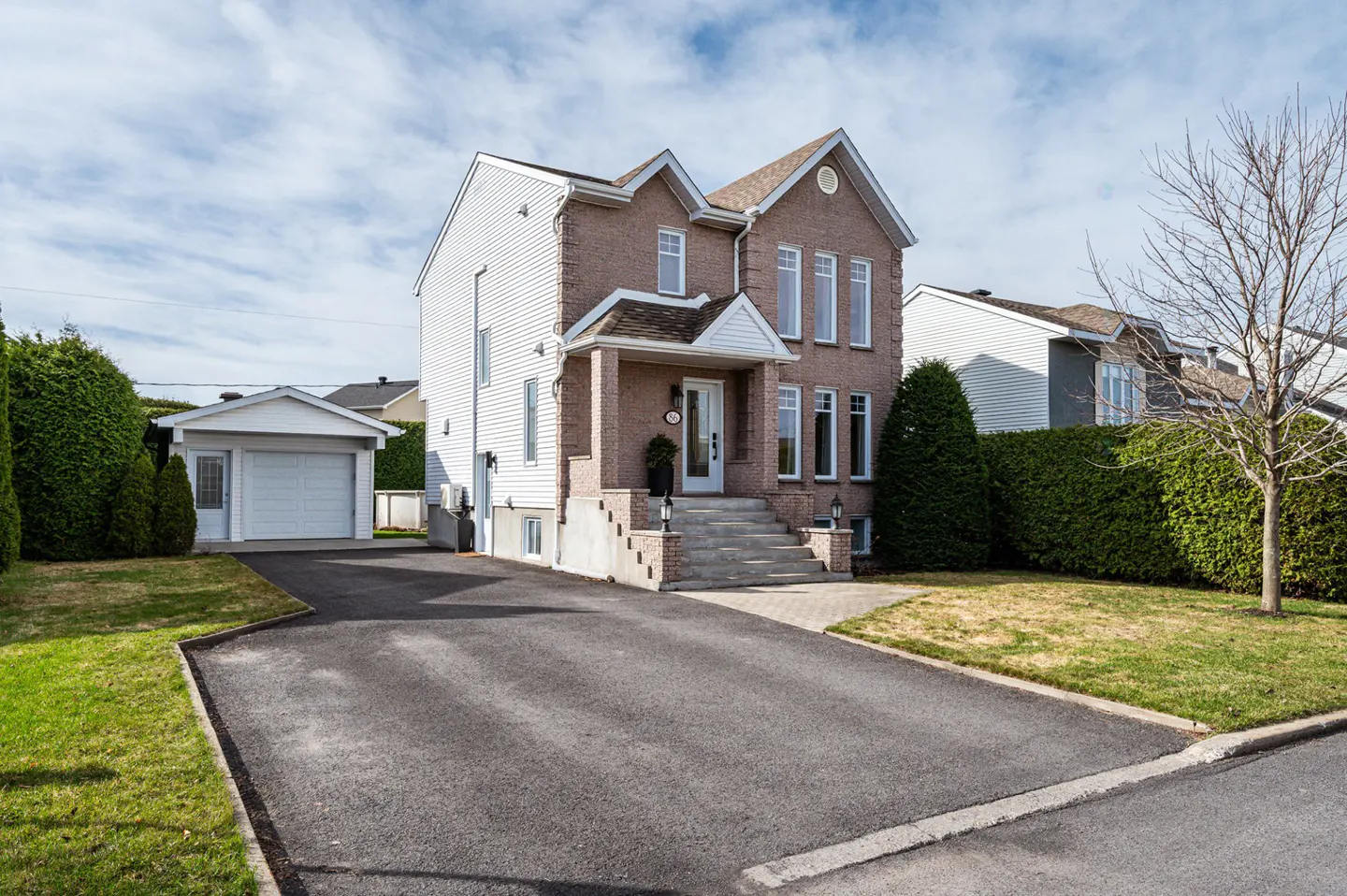 Two-story brick house with white trim, a front porch, and a long driveway leading to a detached garage.
