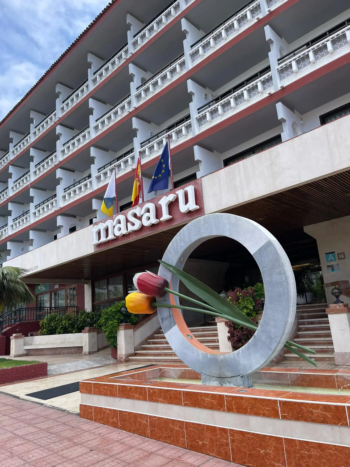 Exterior view of the Masaru Hotel, featuring flags, a flower sculpture, and multiple balconies.