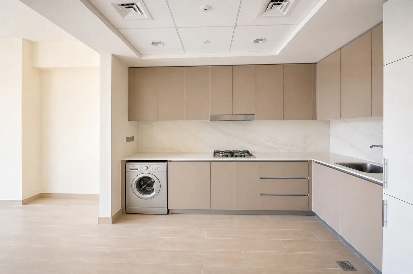 A modern kitchen with beige cabinets, white countertops, and a stainless steel washing machine.