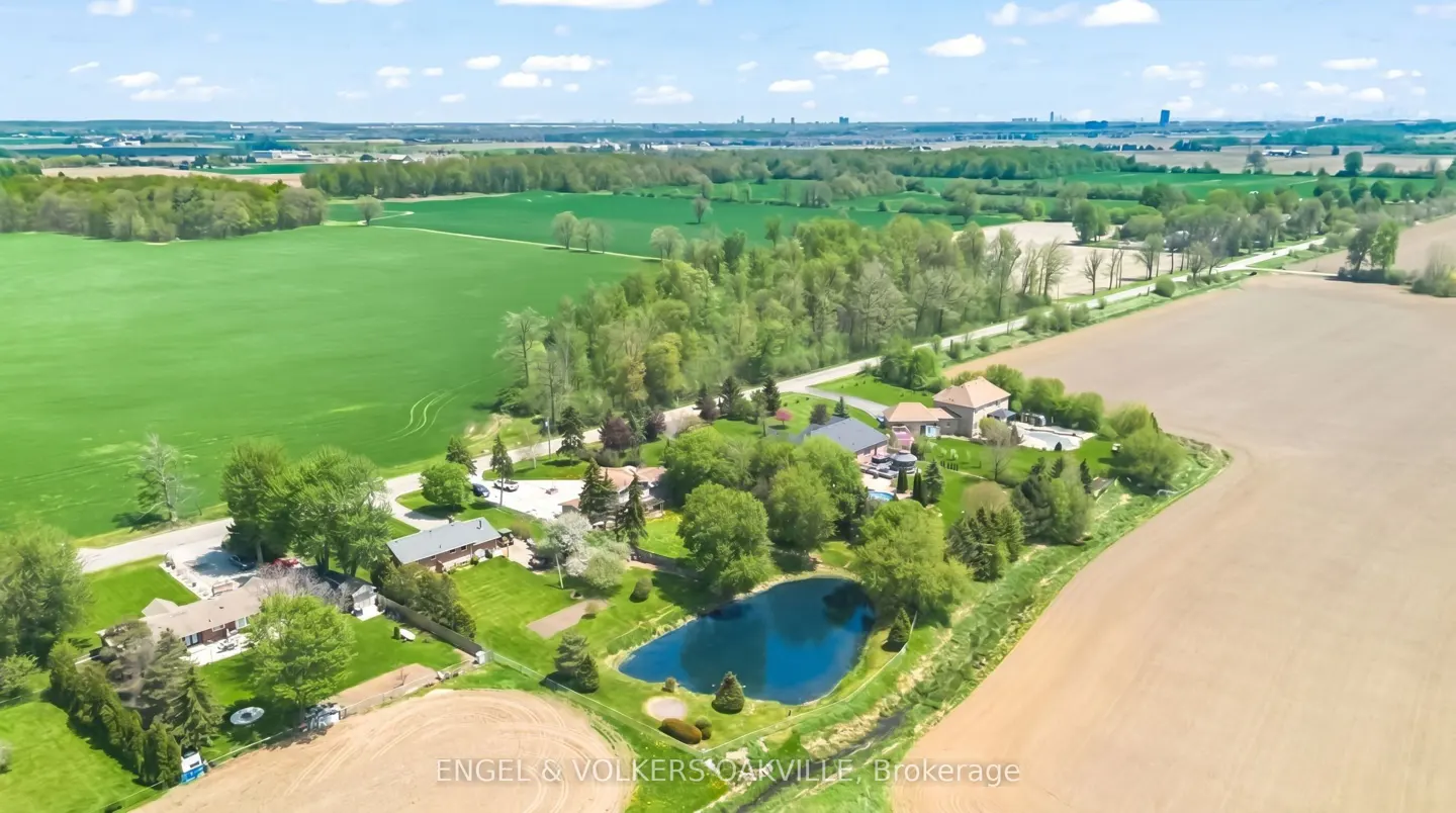 Aerial view of a rural property with houses, a pond, green fields, and brown farmland under a blue sky.