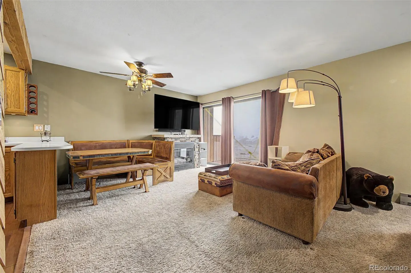 Cozy living room with a brown sofa, wooden table, and a fireplace under a TV. A black bear statue sits near a floor lamp.