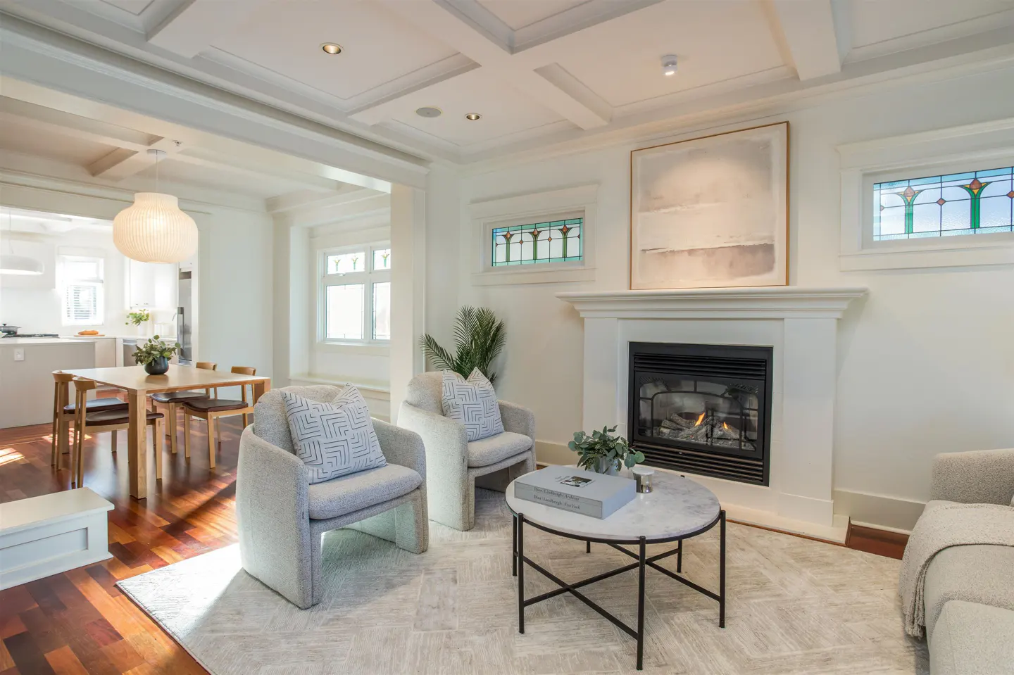 Bright living room with two gray chairs, a fireplace, and a marble coffee table. Dining area visible in the background.