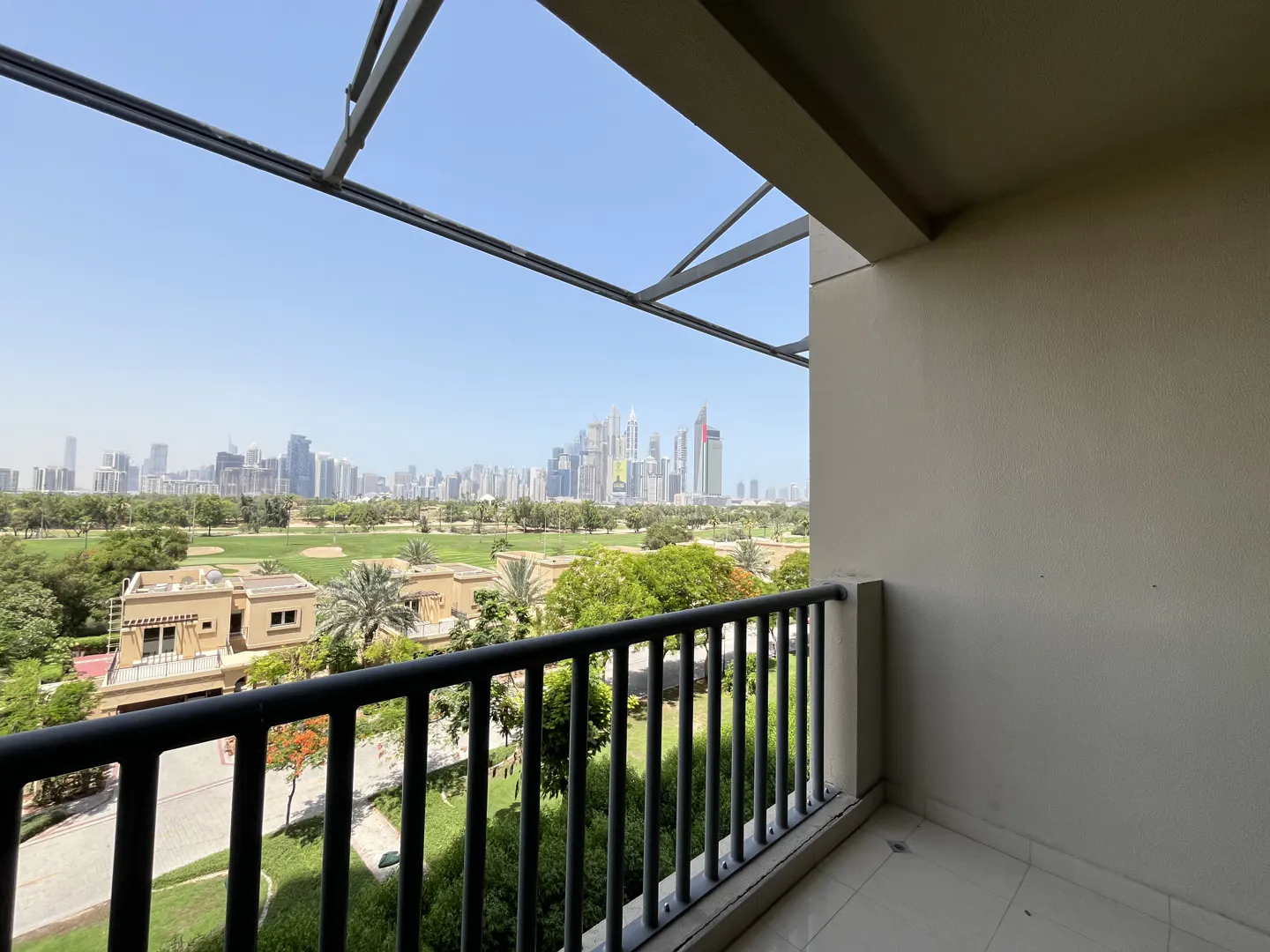 View from a balcony with black railings overlooking a green golf course and a city skyline in the distance.