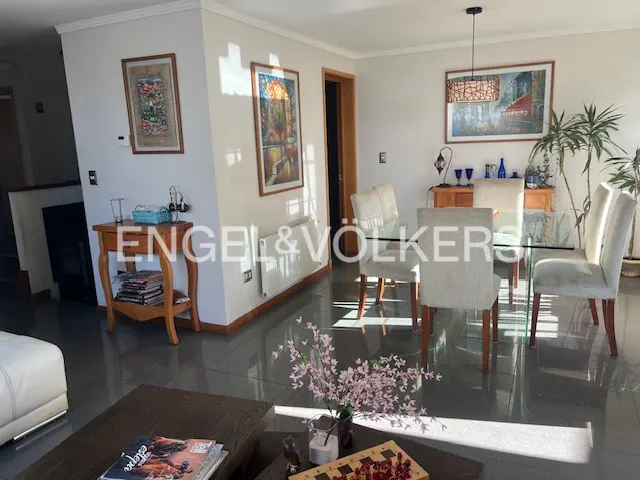 A bright living room with a glass dining table, upholstered chairs, and artwork on the walls.