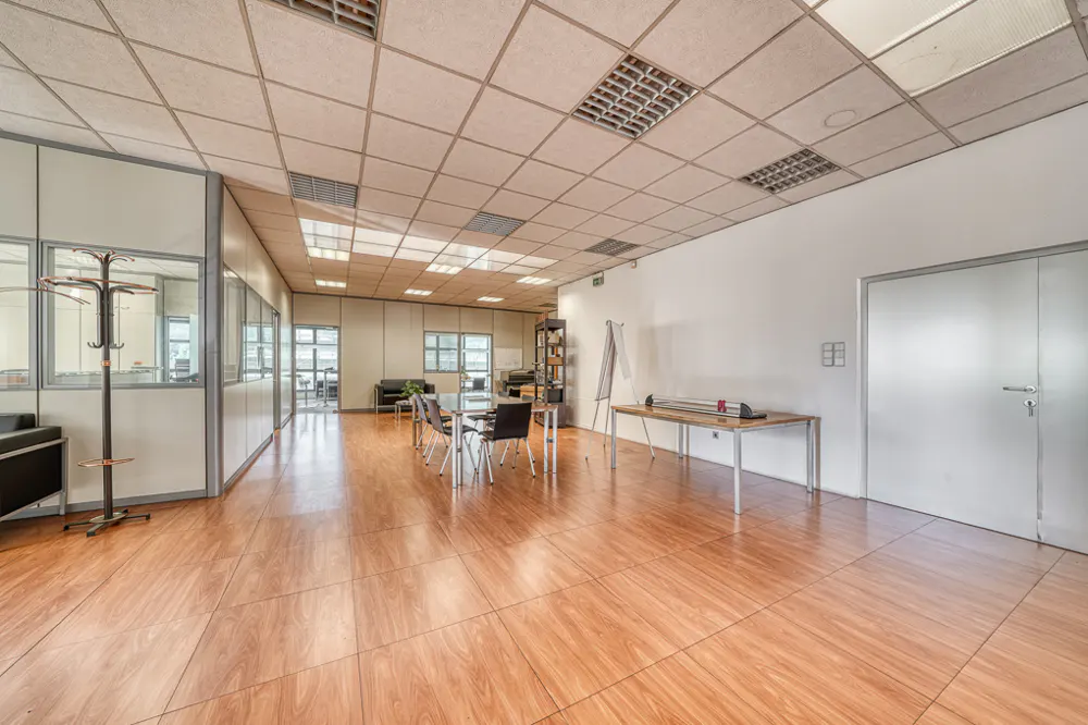 A bright, empty office space with wood floors, a conference table, and a white wall with a door.