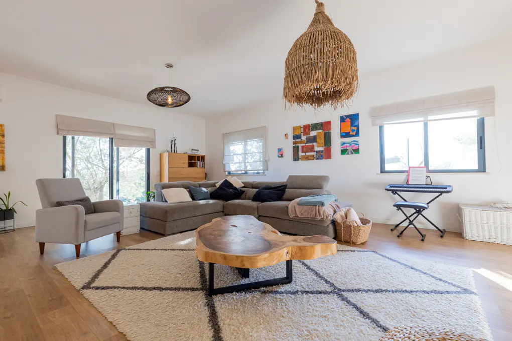 Bright living room with a gray sectional sofa, a wood coffee table, and a gray armchair on a patterned rug. Wicker light fixtures hang from the ceiling.