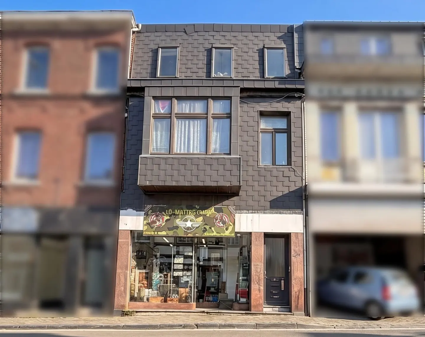 Three-story building with a shop on the ground floor, gray shingle siding, and a black door.