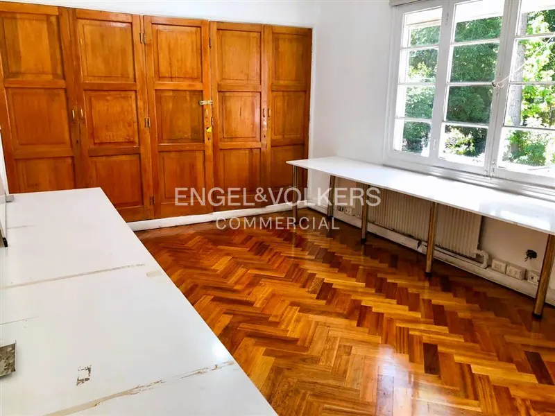Bright office space with herringbone wood floors, white tables, and large windows. Wooden closet doors line one wall.