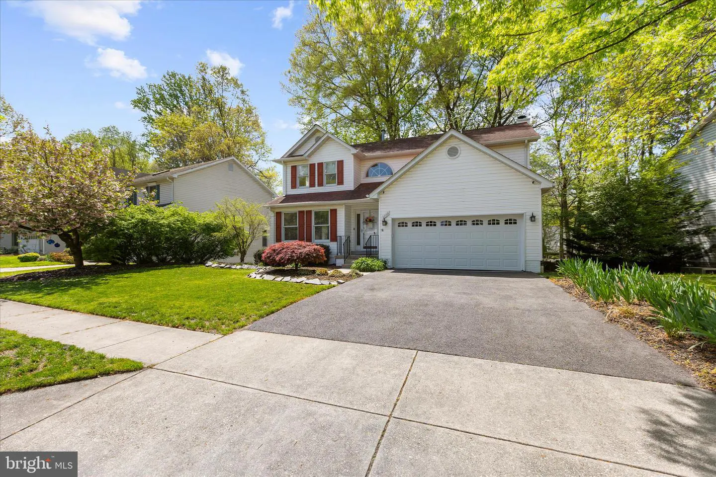 Two-story white house with red shutters, a two-car garage, and a green lawn on a sunny day.