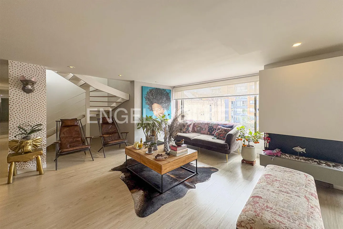 Living room with a brown sofa, wooden coffee table, and a large blue painting. A white staircase is visible in the background.