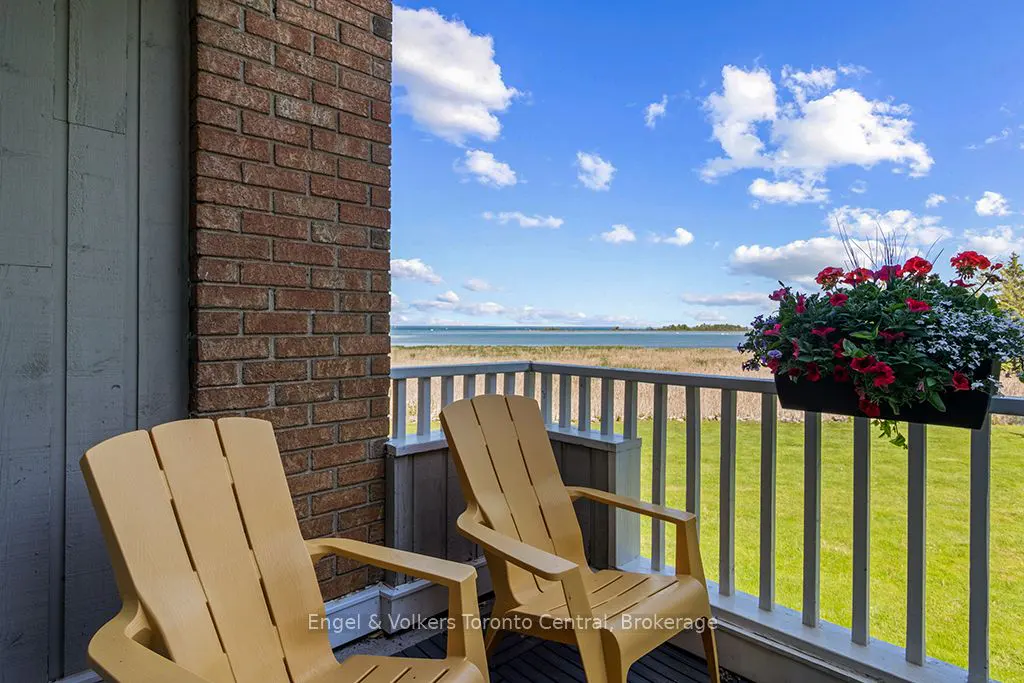 Two yellow Adirondack chairs on a balcony overlooking a grassy lawn, a lake, and a bright blue sky with white clouds.