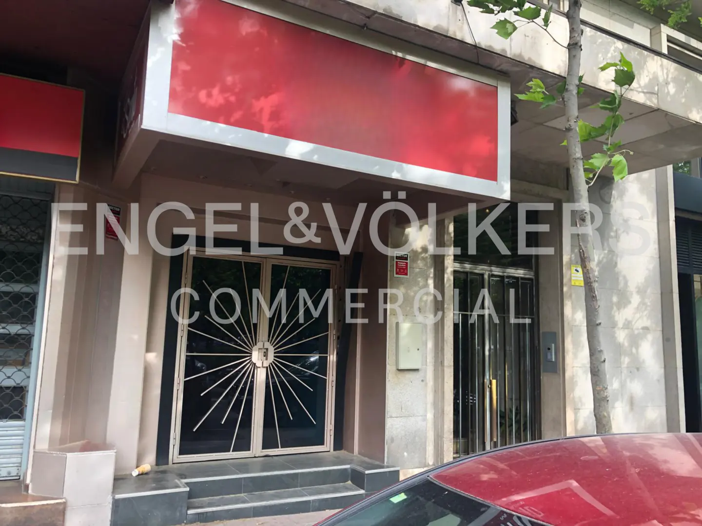 Exterior of a commercial building with a red sign and metal doors. The Engel & Völkers logo is superimposed on the image.