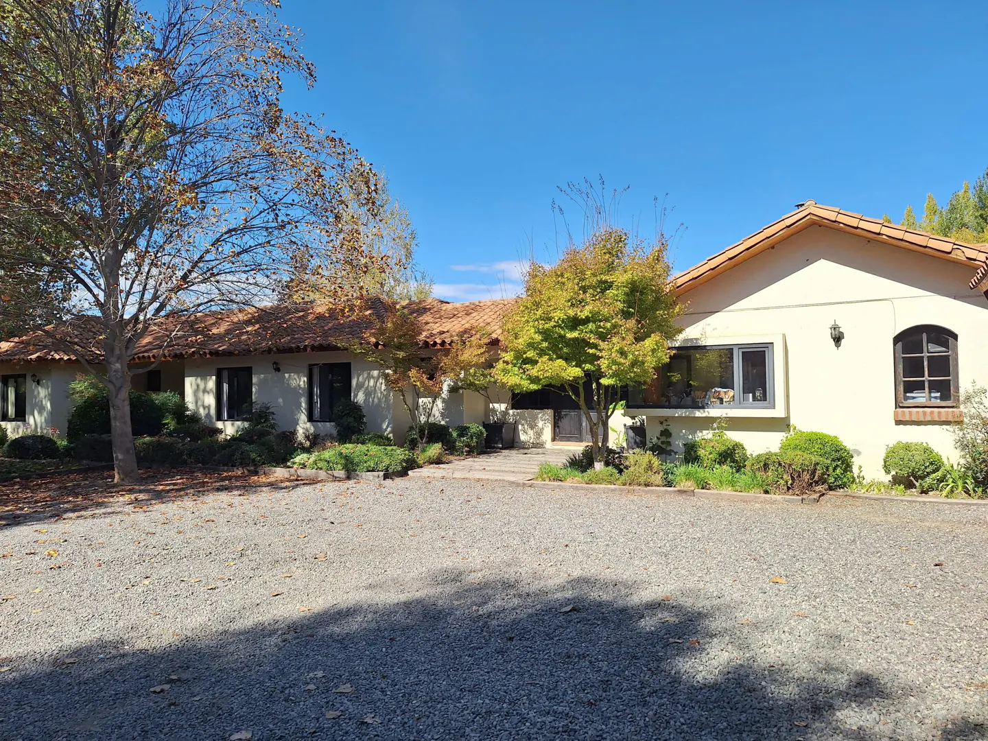 A single-story home with a red tile roof, cream-colored walls, and black-framed windows. Trees are in the front yard.