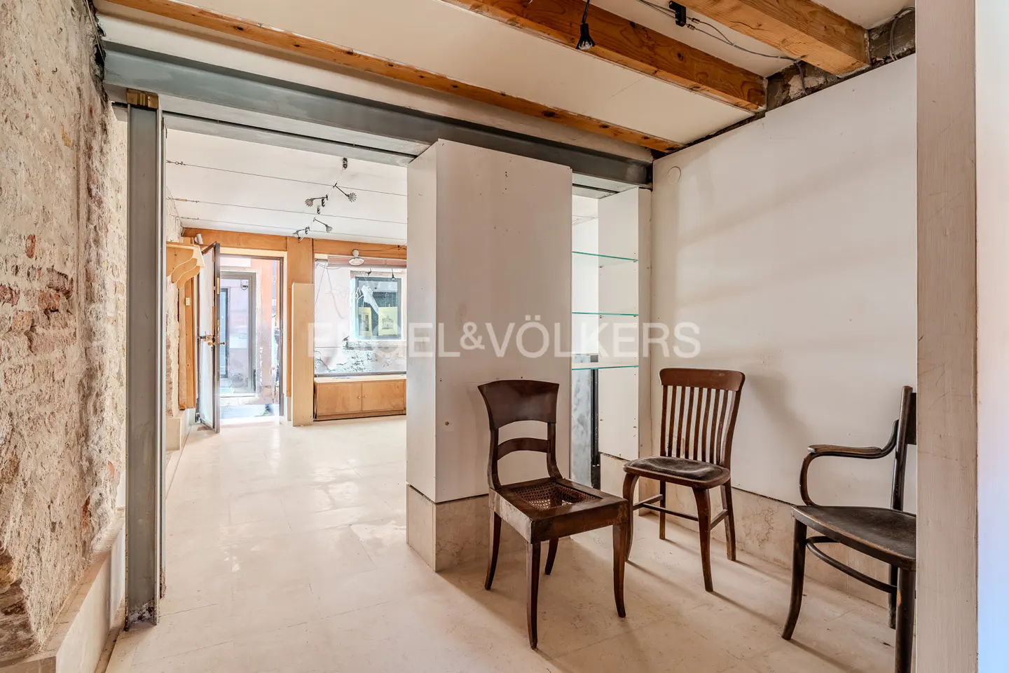 Interior view of a room with exposed brick, wooden beams, and three wooden chairs.