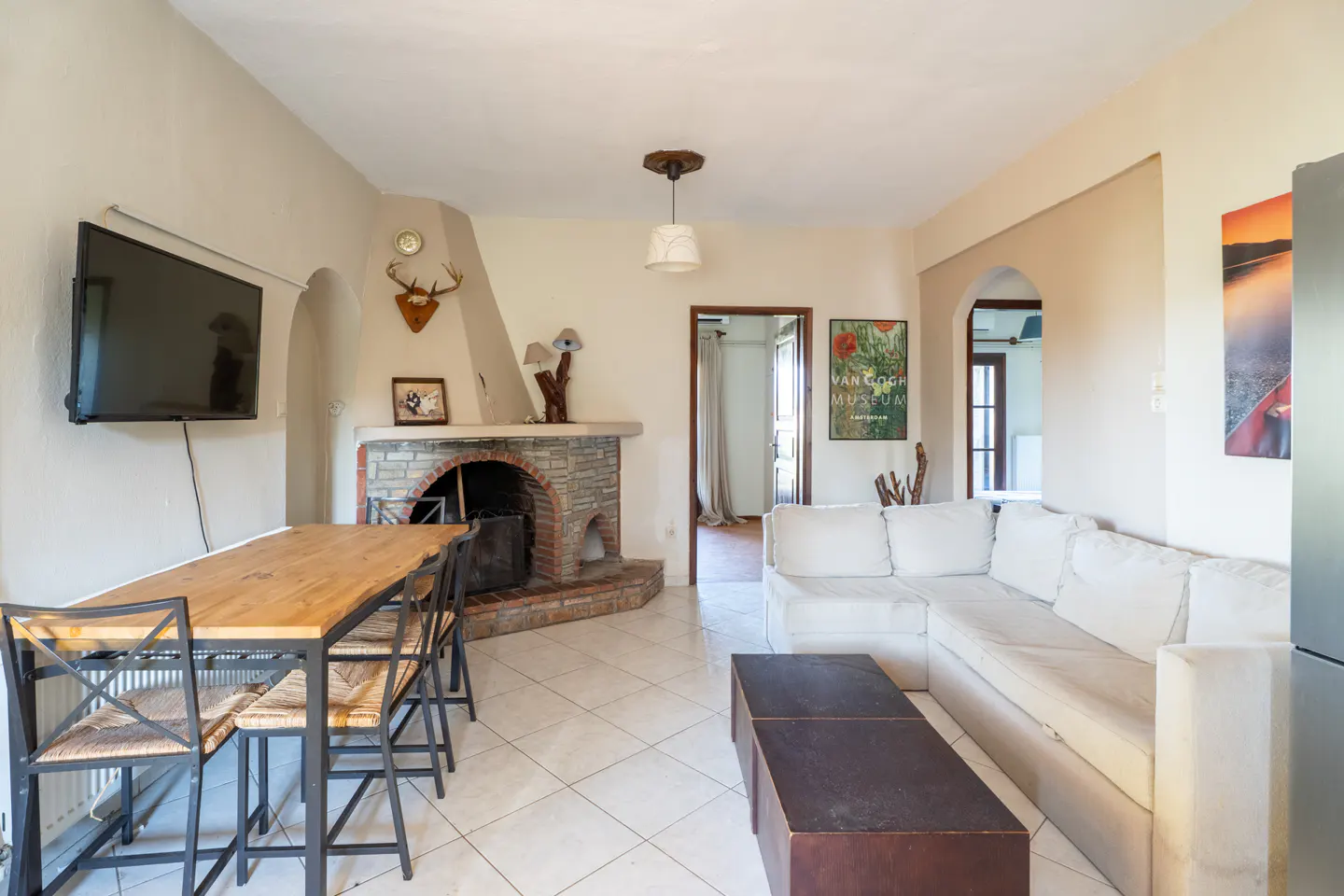 Bright living room with white tile floor, stone fireplace, wood table with chairs, and white sectional sofa.