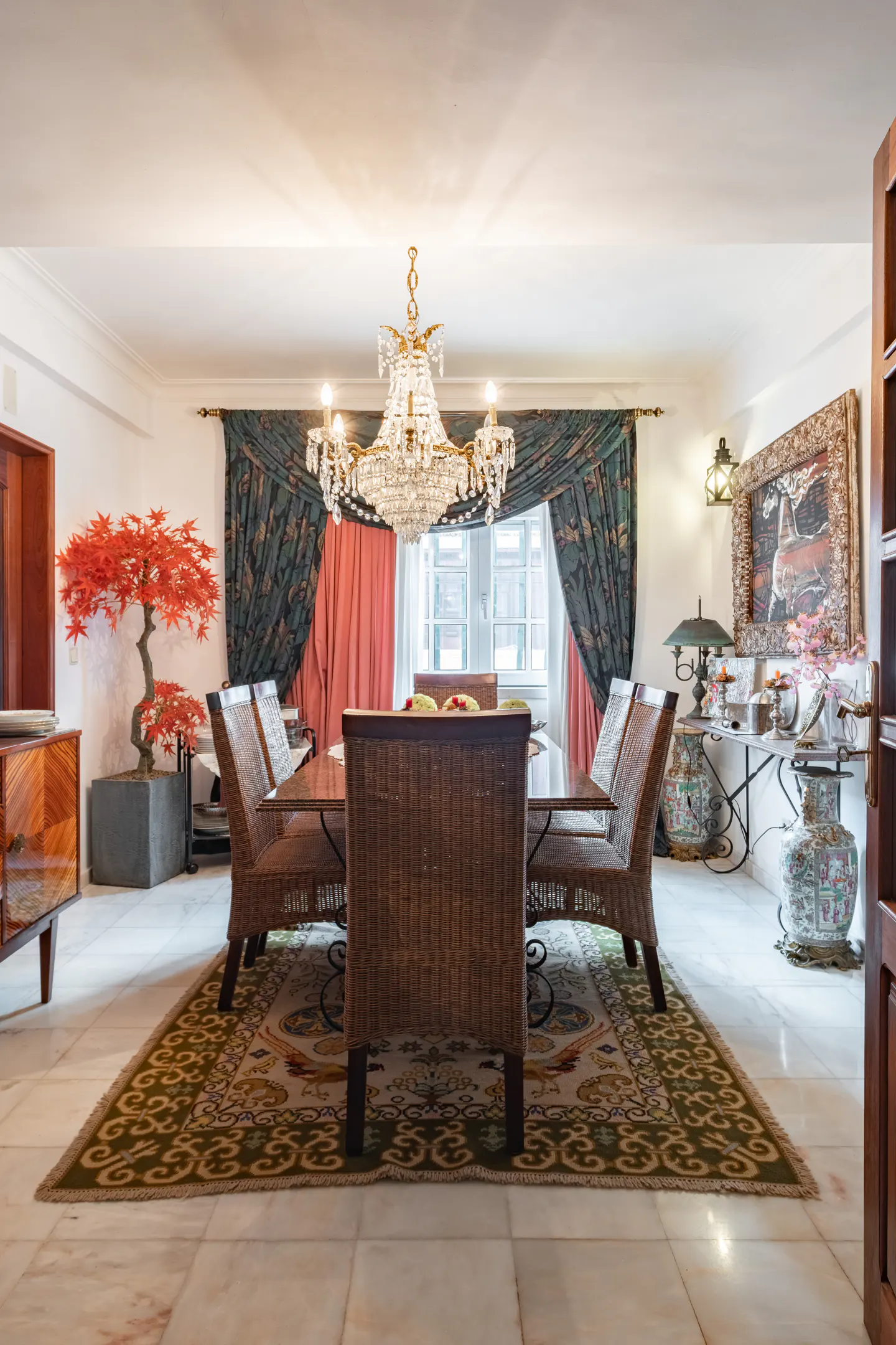 A dining room with a table, wicker chairs, a chandelier, and a patterned rug.