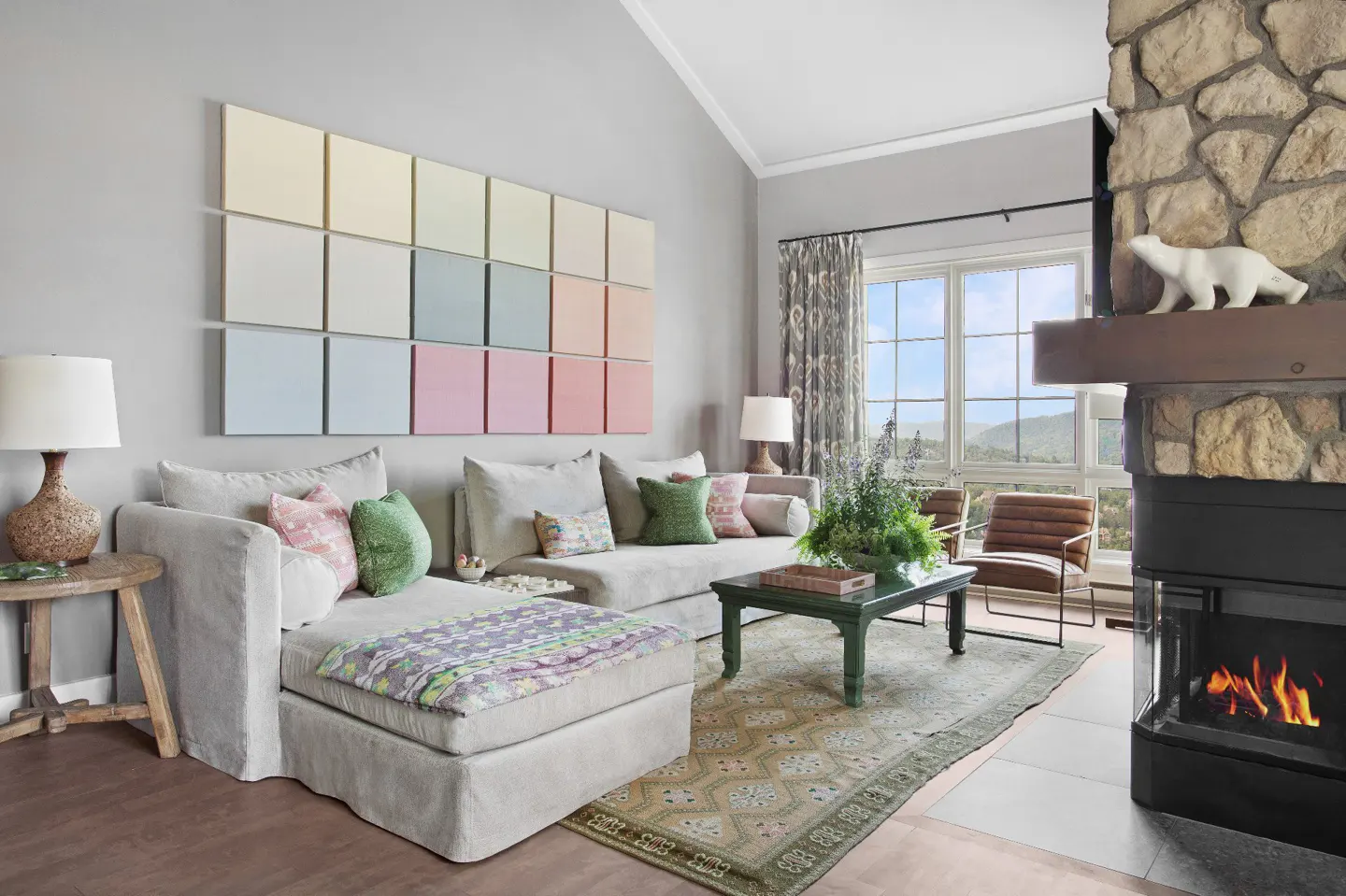 Living room with gray sofa, colorful square wall art, stone fireplace, and mountain view.