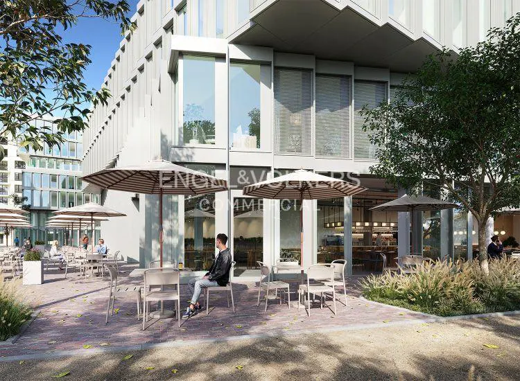 Outdoor cafe with striped umbrellas and seating in front of a modern building with large windows. Engel & Volkers Commercial logo visible.