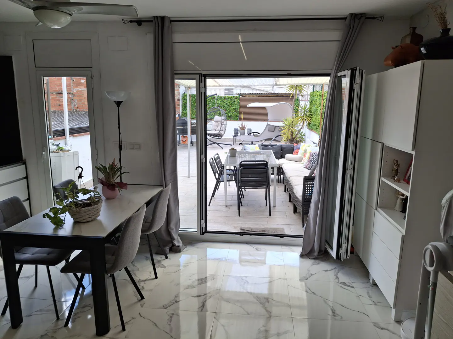 Dining room with marble floors and table, opening to a patio with outdoor seating, a dining set, and a hanging chair.