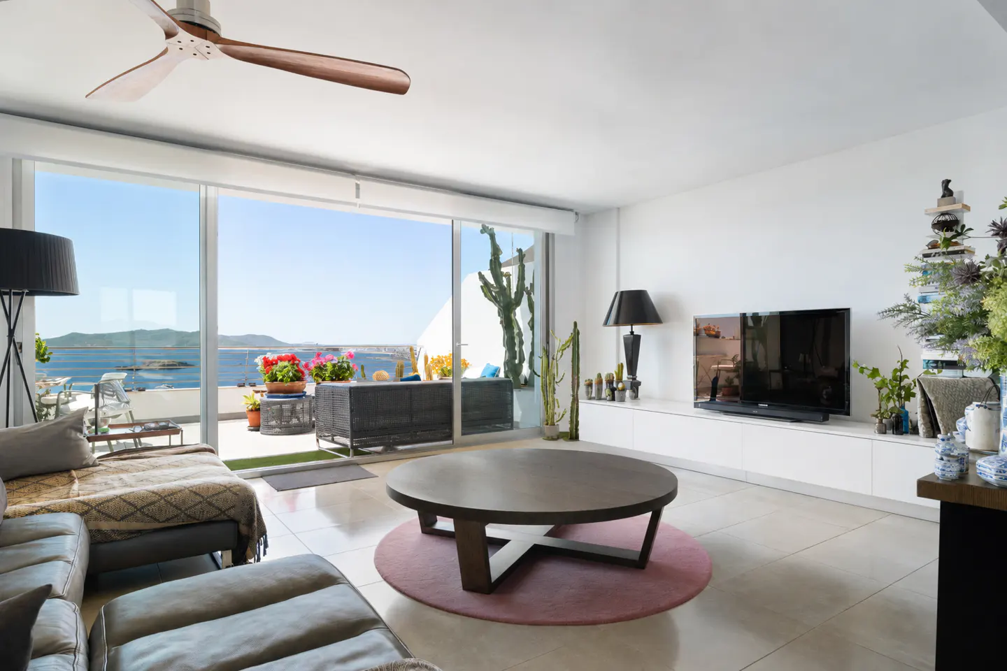 Modern living room with a round coffee table, grey sofa, and large sliding doors opening to a balcony with ocean views.