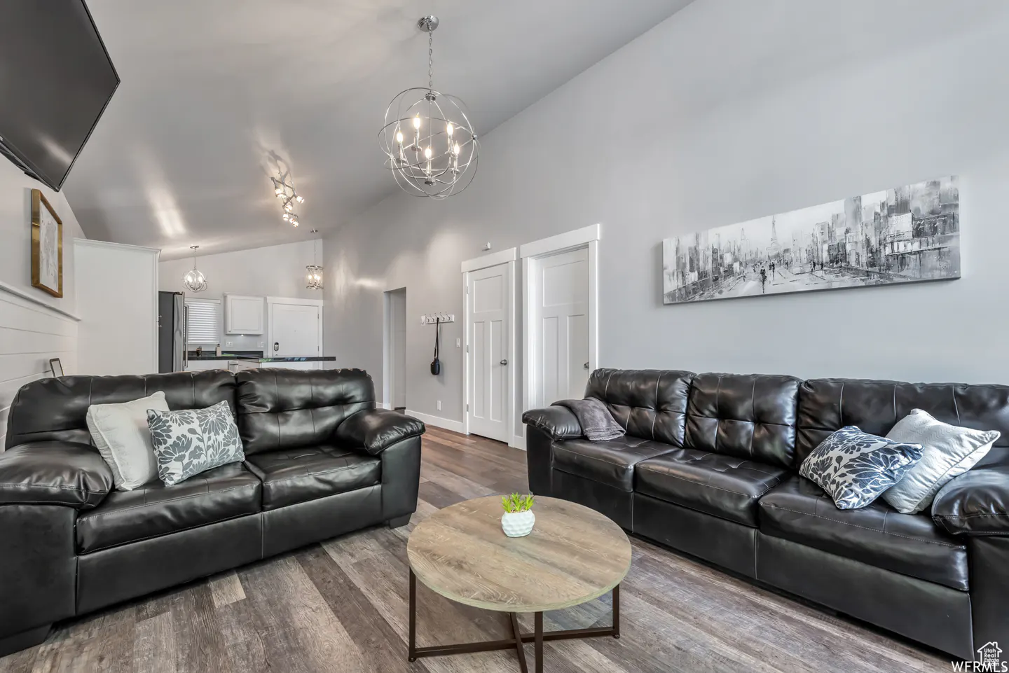 Living room with two black leather sofas, a round coffee table, and gray walls. A black and white city painting hangs above the sofa.