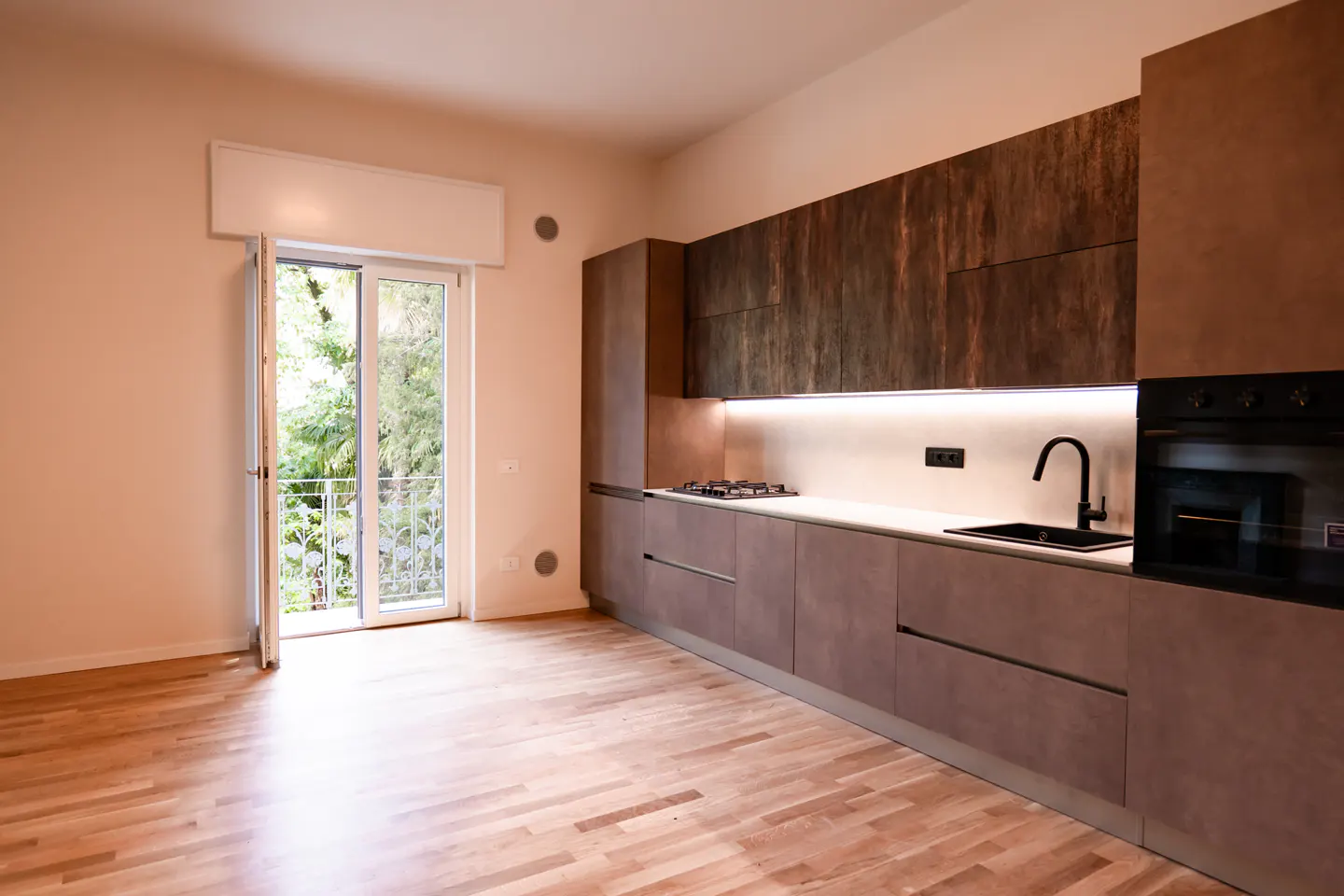Modern kitchen with dark wood cabinets, light countertops, and hardwood floors, featuring a door to a balcony.
