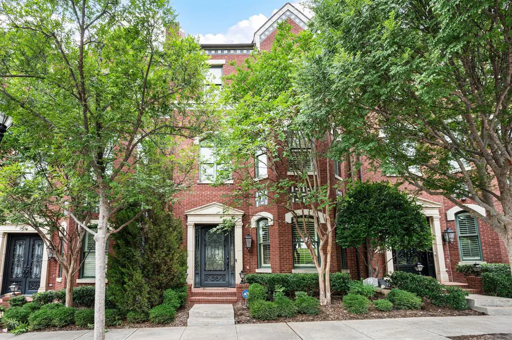Brick townhouses with black doors and green trees on a sunny day.