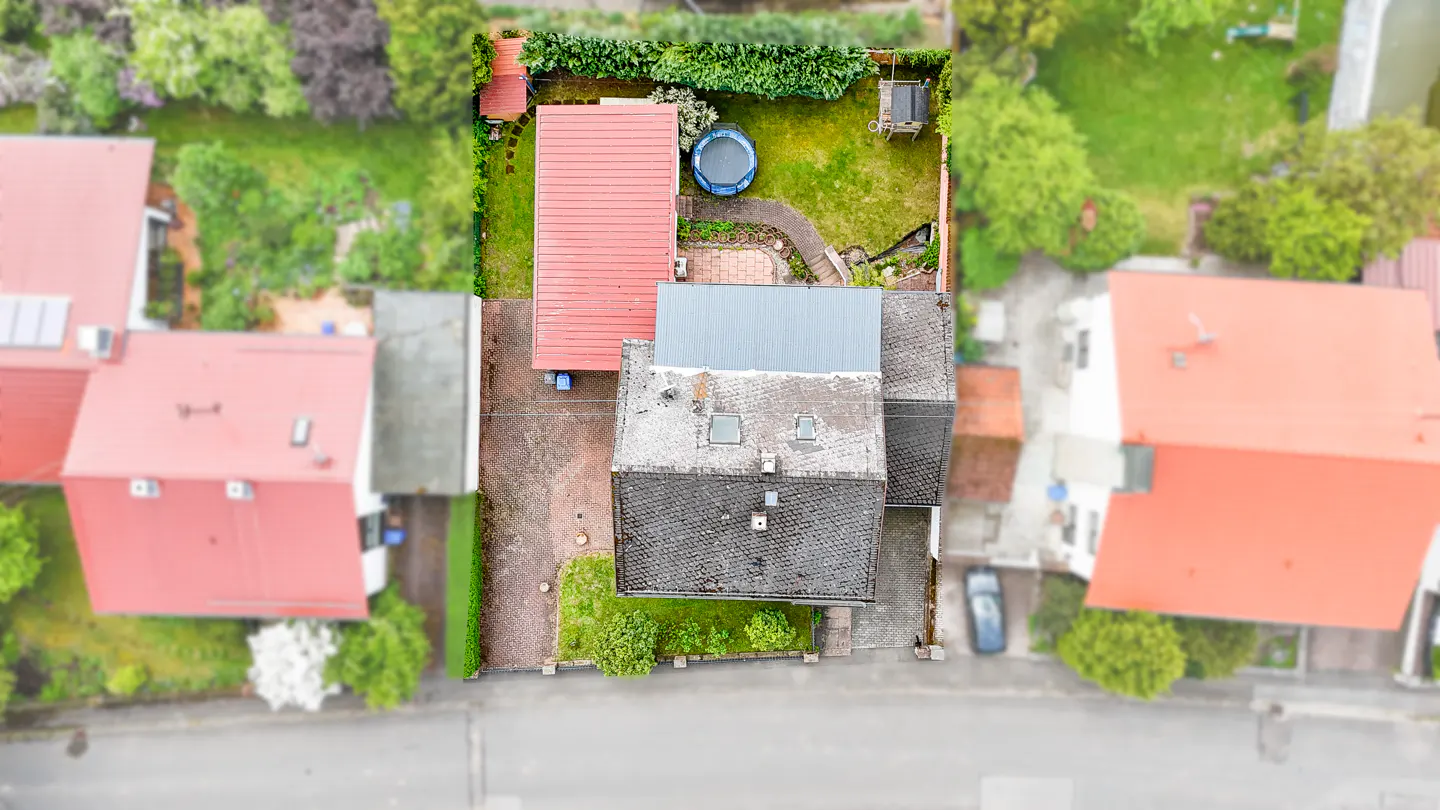 Aerial view of a house with a red roof, a green lawn, and a blue inflatable pool in the backyard.