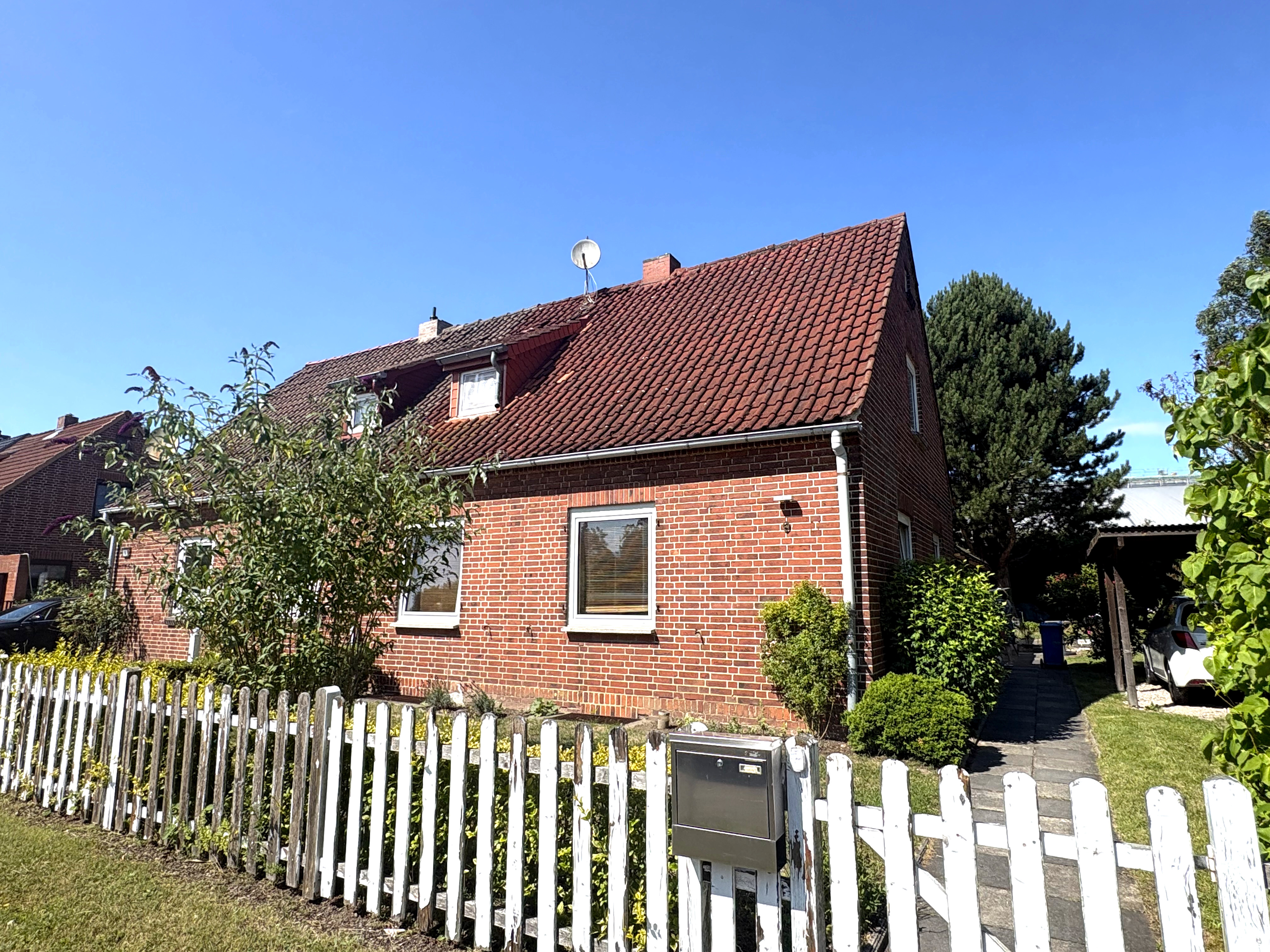 A red brick house with a tiled roof and white picket fence under a clear blue sky. [AI-generated text]