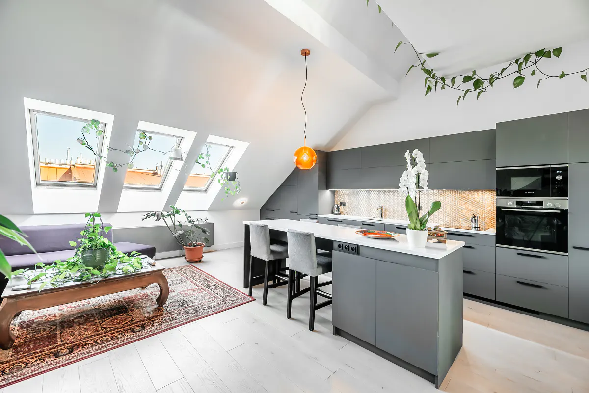 Modern attic kitchen with grey cabinets, a white island, bar stools, and a cozy seating area with a patterned rug.