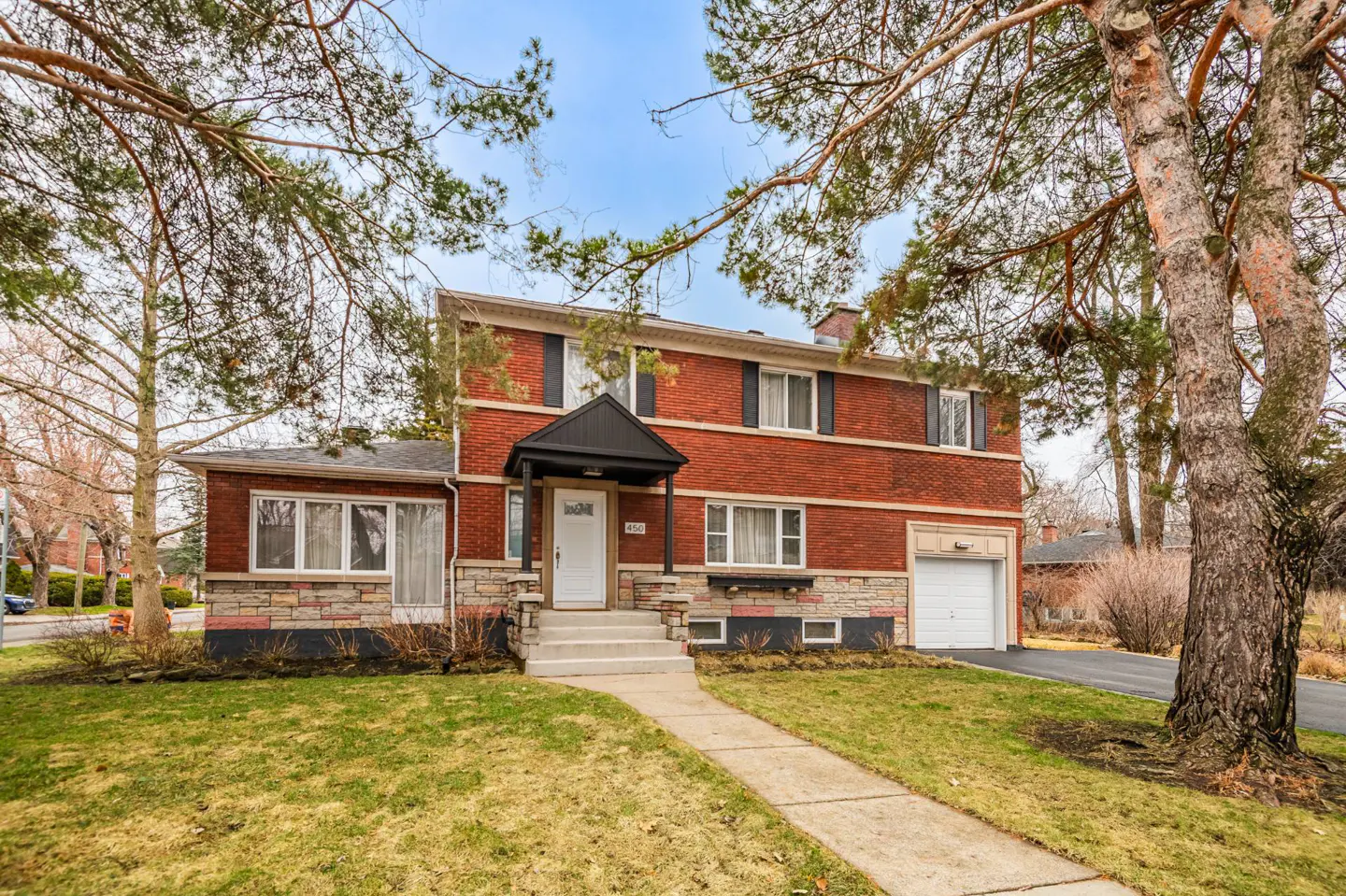 Two-story red brick house with a white door, black shutters, and a small garage on a green lawn.