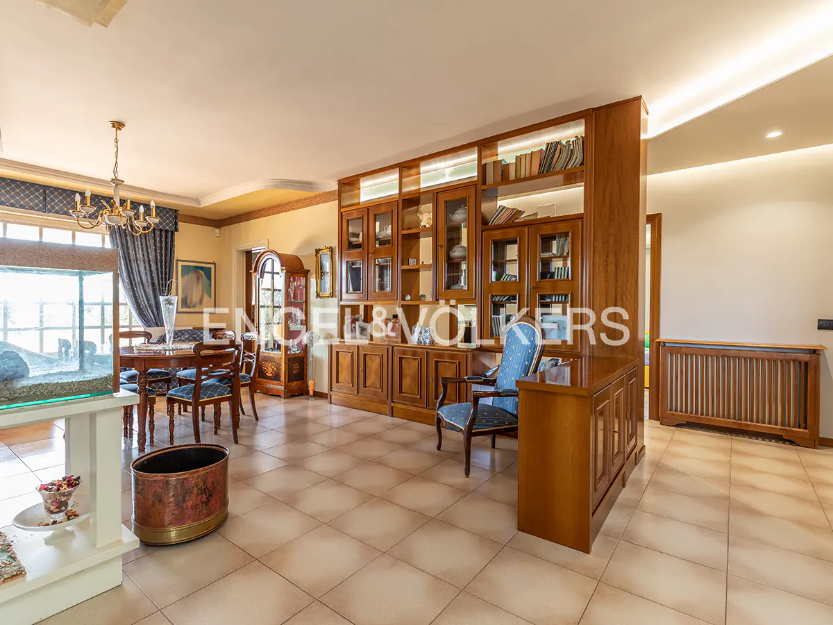 A spacious living room with a dining area, a large wooden bookcase, and tiled floors.