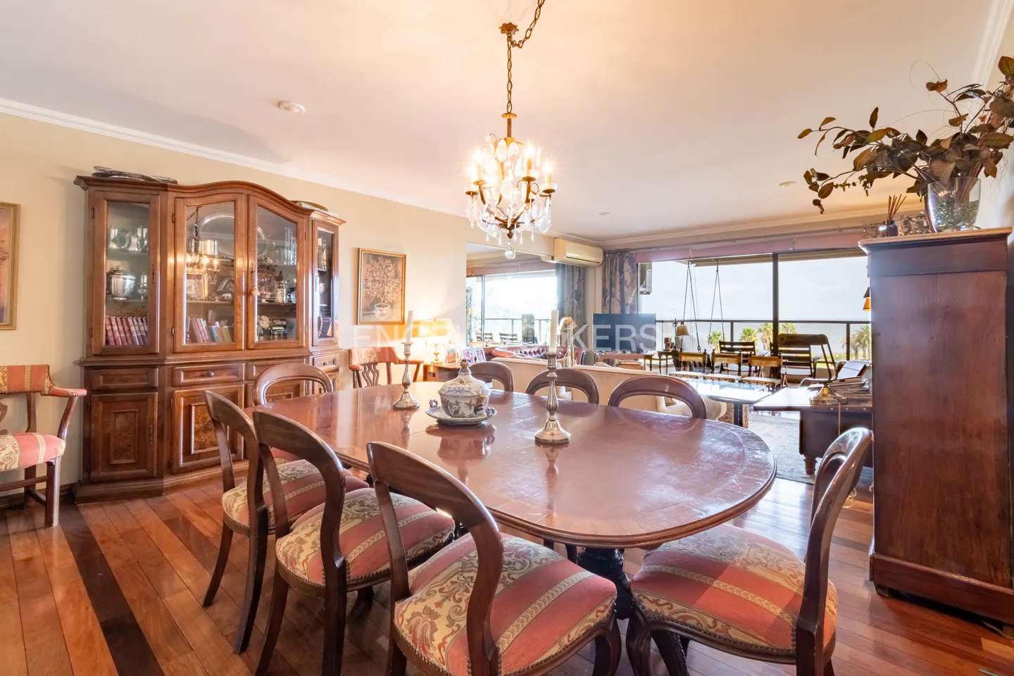 Formal dining room with a wooden table, patterned chairs, a crystal chandelier, and a view of a balcony through glass doors.