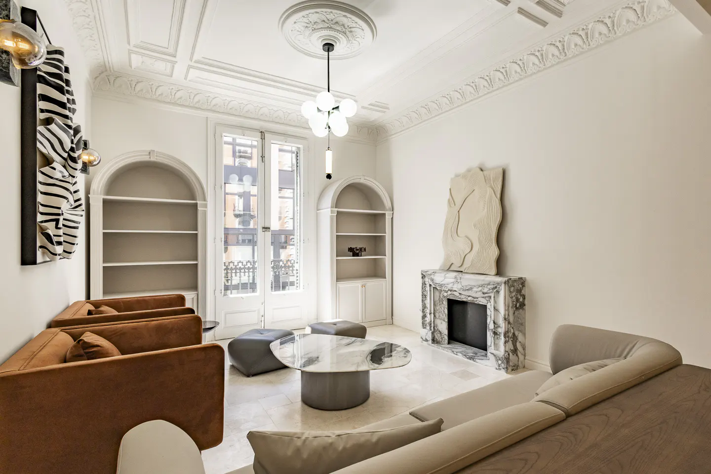 Bright living room with white walls, marble fireplace, and arched bookshelves. Brown sofas and a marble coffee table add warmth to the space.