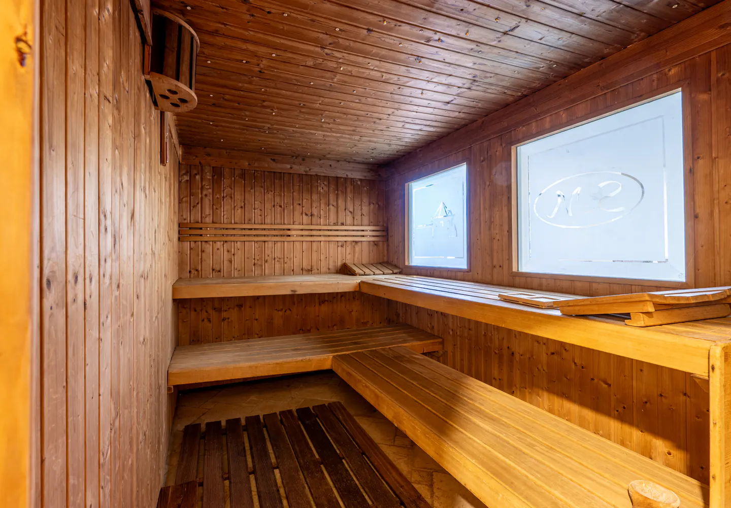 Interior view of a wooden sauna with benches, wood-paneled walls, and two frosted windows.