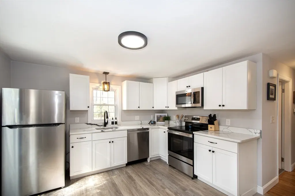 Bright kitchen with white cabinets, stainless steel appliances, and light wood-look flooring. A window sits above the sink.