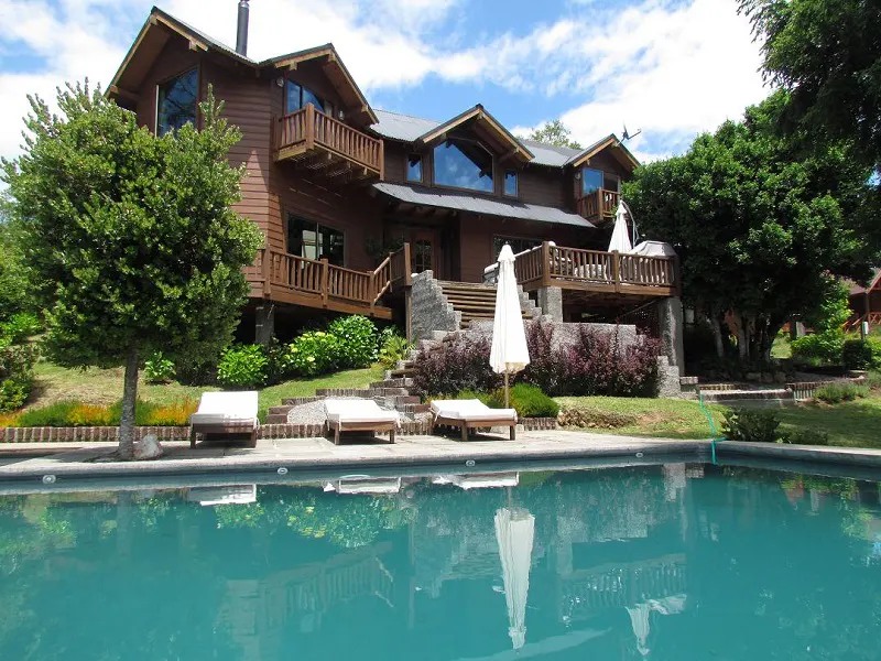 A brown, multi-story house with balconies overlooks a pool with lounge chairs.