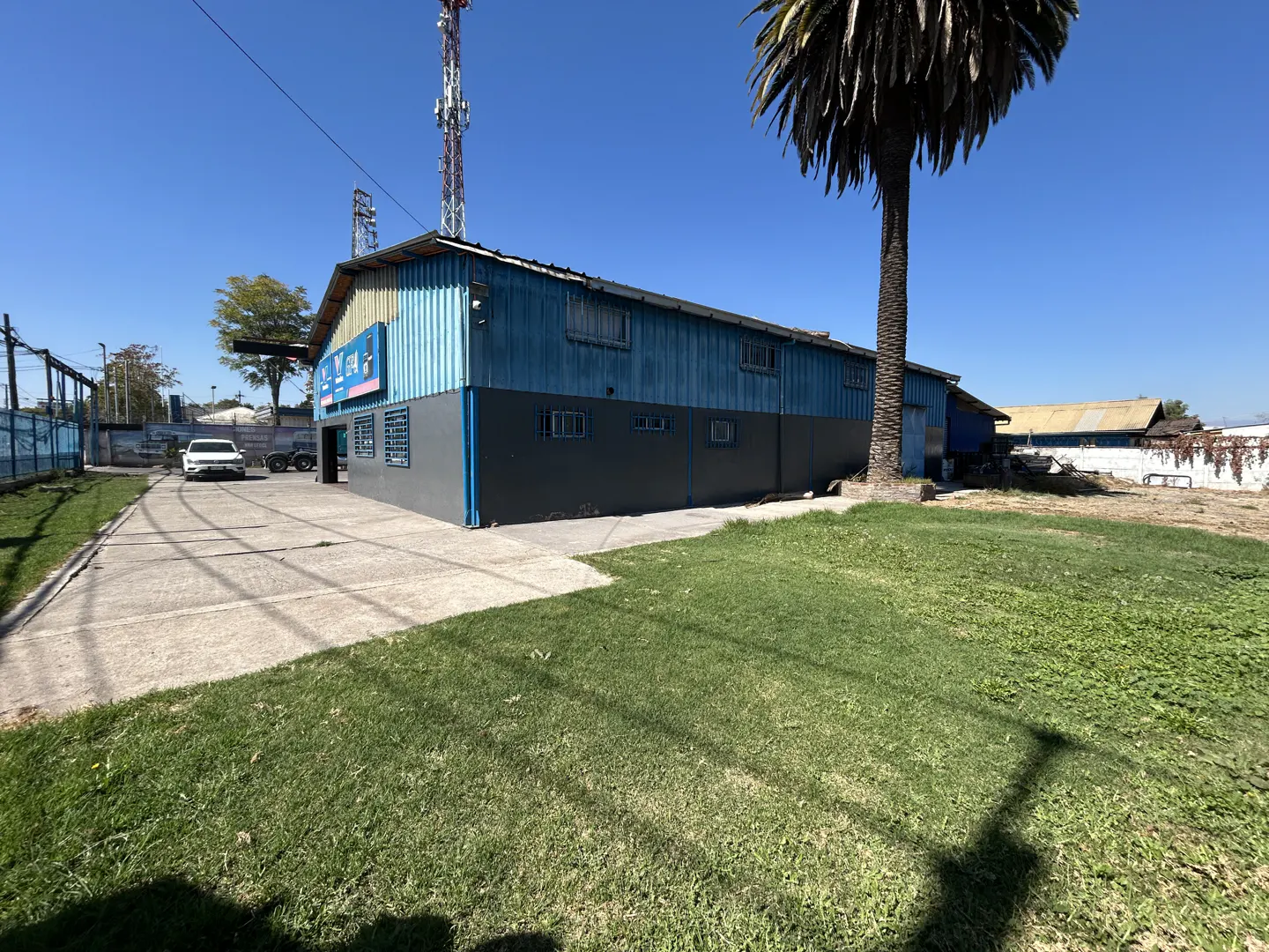 Exterior of a blue and gray warehouse building with a palm tree and green lawn in front. A white car is parked nearby.