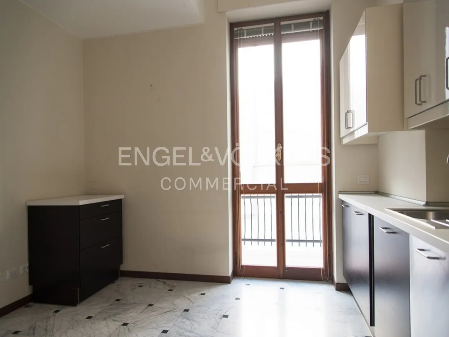 A bright kitchen with marble floors, dark cabinets, and a door to a balcony.