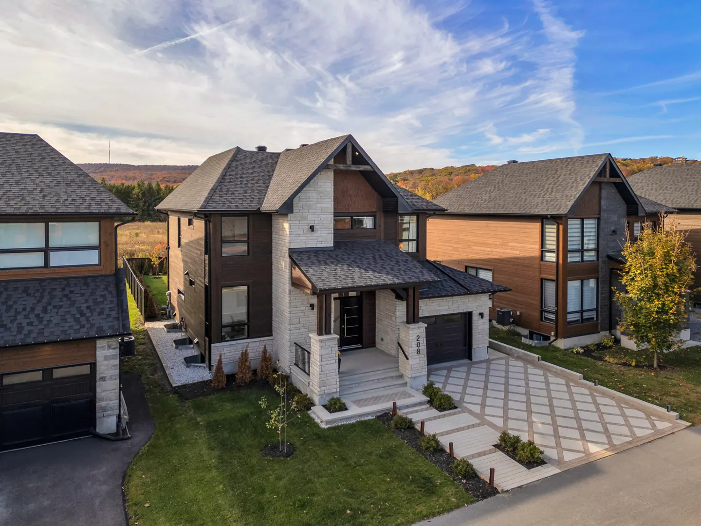 Two-story house with stone and dark brown wood exterior, black roof, and patterned driveway.