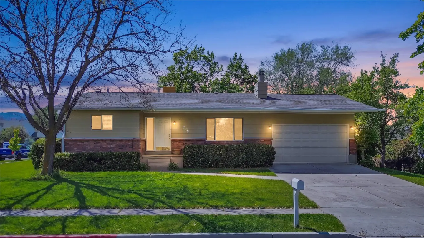 A single-story home with a green lawn, brick accents, and an attached garage at dusk.