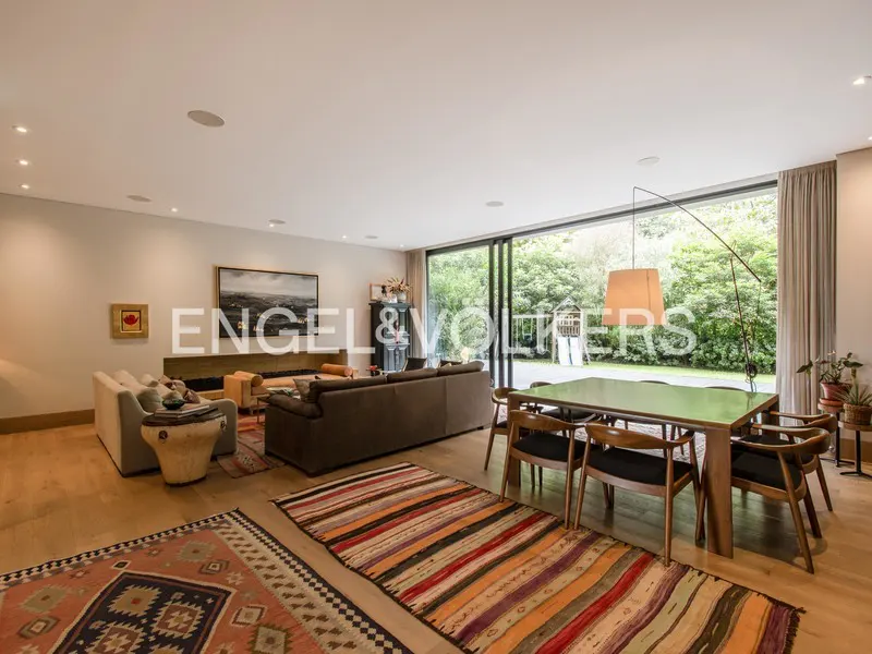 Open-concept living and dining room with wood floors, sofas, and a large glass door to the backyard. Colorful rugs add warmth.