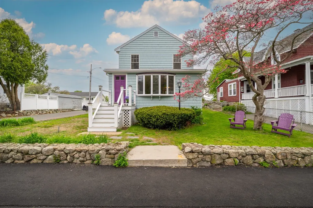 A two-story light blue house with a purple door, white stairs, and a stone wall in front.