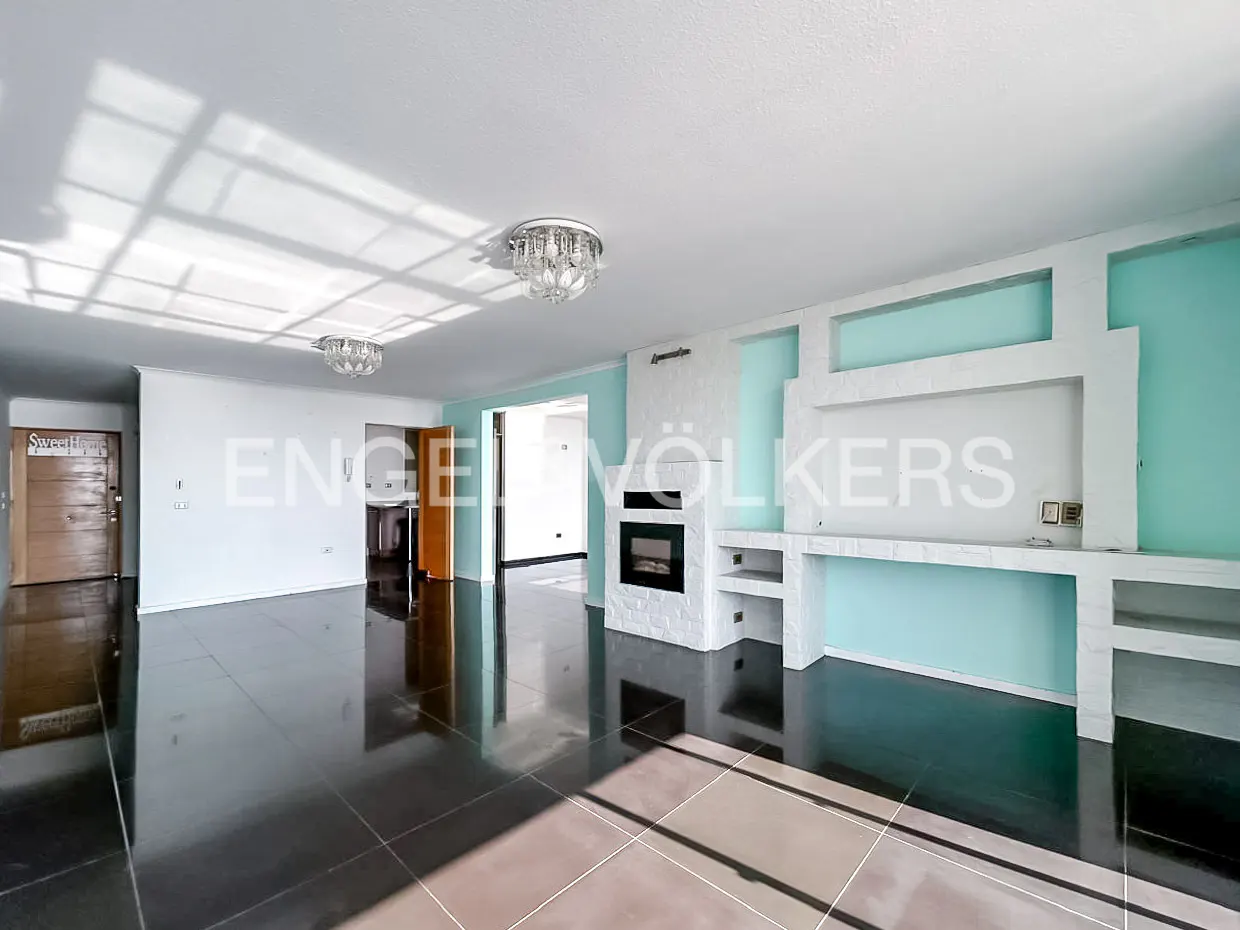 A bright living room with black tile floors, a white fireplace, and light blue accent walls. Chandeliers hang from the white ceiling. Doors lead to other rooms.